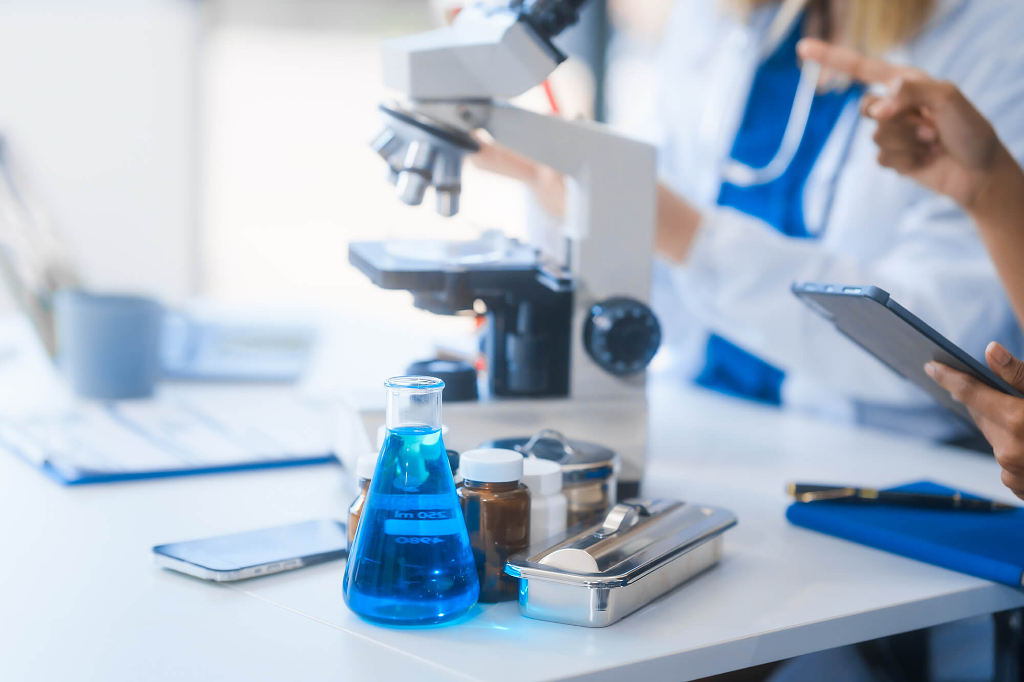 Three scientists discussing while standing around a microscope and some samples